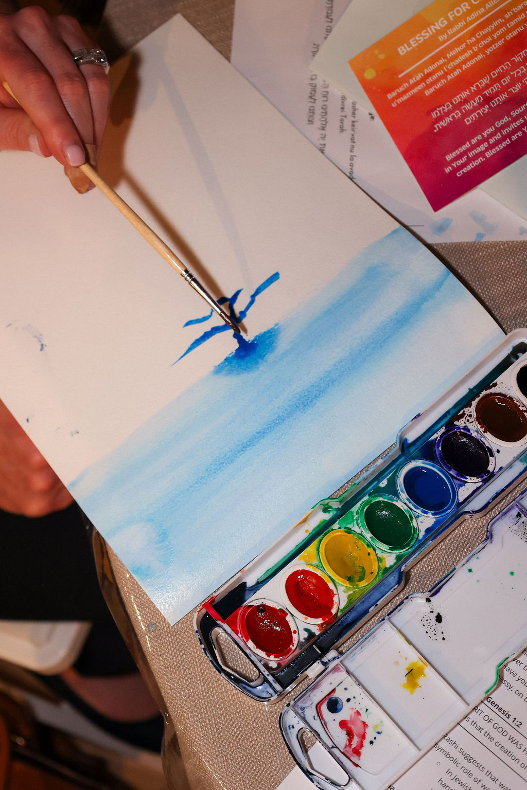 Person painting a watercolor scene at a Maaleh Hayim gathering